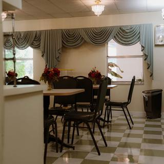 A cozy dining room with checkered flooring, adorned with elegant curtains and flower arrangements on the tables.