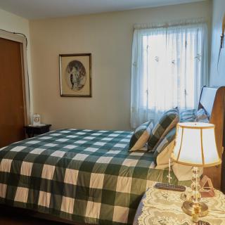 A cozy bedroom with a checkered bedspread, a bedside lamp, and a window allowing natural light.