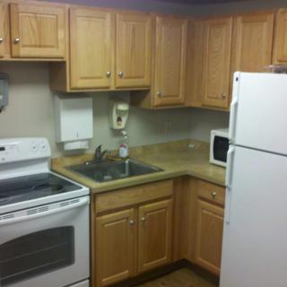 A compact kitchen with wooden cabinets, an oven, refrigerator, microwave, and sink.