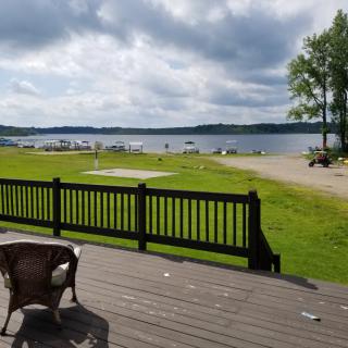 A scenic lakeside view with a deck, chairs, and a cloudy sky.