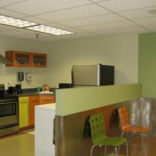 A modern office kitchen with stainless steel appliances and colorful chairs.