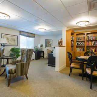 A cozy office space featuring a seating area with armchairs and a table, alongside a bookshelf filled with books.