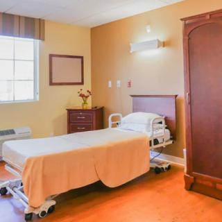 A well-lit hospital room with a single bed and wooden furniture.