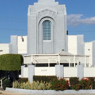 A striking modern building with a prominent arch window, surrounded by well-maintained landscaping under a clear blue sky.