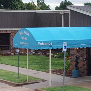 A building entrance with a blue canopy awning and nearby parking signs.