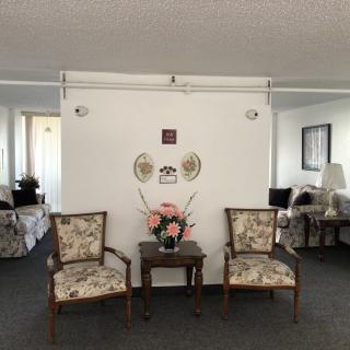 A living room seating area with two decorative chairs and a small table adorned with flowers, set against a white wall with framed artwork.