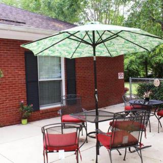 A cozy patio setup with a table and red-cushioned chairs under a green umbrella, set against a brick house backdrop.