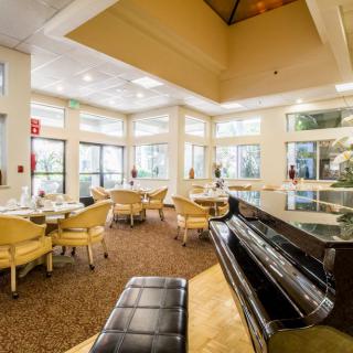 A spacious lounge with a piano and seating area, featuring large windows and elegant interior design.