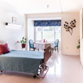 A well-lit hospital room featuring a patient bed, chairs, and decorative elements.