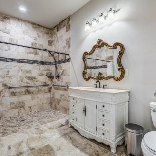 A rustic yet elegant bathroom featuring a large walk-in shower, ornate mirror, and vintage-style vanity.