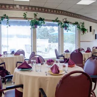 An interior view of a restaurant dining area with tables set and decorated with napkins near large windows.