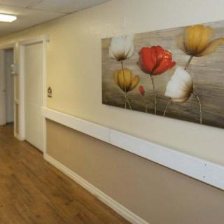 A hallway with wooden flooring and a floral painting on the wall.