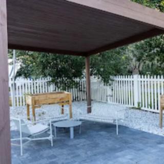 A cozy outdoor patio area with a wooden pergola, surrounded by greenery and featuring comfortable seating.