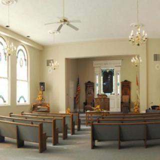 Interior of a church with rows of pews, large windows, and chandeliers.