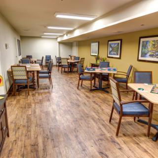 A neatly arranged dining area with tables and chairs, featuring hardwood floors and decorative artwork on the walls.