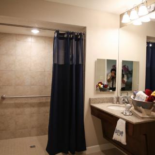 A well-lit bathroom featuring a shower with a navy curtain, a sink area with a mirror, and neatly arranged towels.