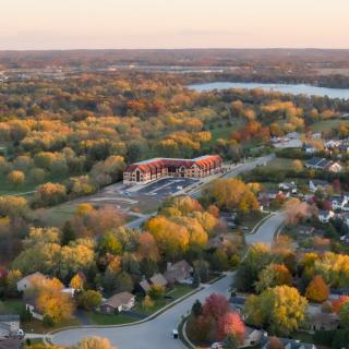 A stunning aerial view of a suburban neighborhood during autumn, showcasing vibrant fall foliage and a tranquil landscape at sunset.