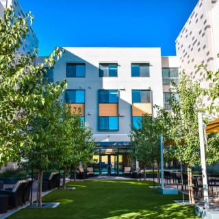A modern urban building surrounded by trees and green space under a clear blue sky.