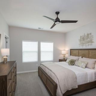 A modern bedroom with neutral tones, featuring a large bed, ceiling fan, and stylish decor.