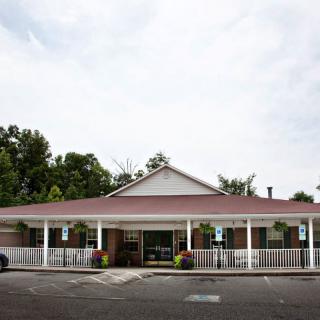 A small restaurant with a covered porch and parking area in front, surrounded by trees under a cloudy sky.