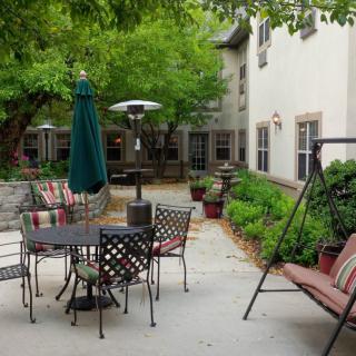 A cozy outdoor patio area with a dining table, chairs, a swing, and lush greenery surrounding the space.