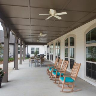A spacious covered porch with rocking chairs and a dining table, featuring ceiling fans for comfort.