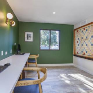 A modern workspace featuring a green accent wall, natural light, and stylish furnishings.