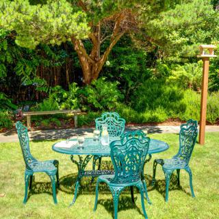 A picturesque garden setting with ornate green patio furniture surrounded by lush greenery.