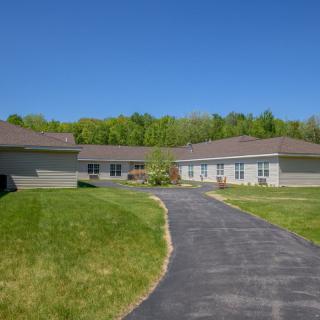 A modern, single-story building surrounded by lush green grass and trees under a bright blue sky.
