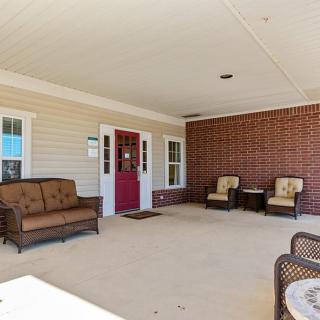 An inviting covered patio area with comfortable seating, including a sofa and chairs against a backdrop of brick and siding.