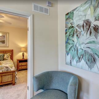 A cozy bedroom with a view through an open doorway, featuring a decorative chair and a large piece of artwork on the wall.