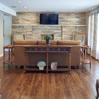 A cozy living room with a sofa, wood flooring, and a wall-mounted television.