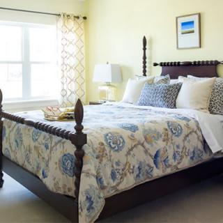 A cozy bedroom with a wooden bed frame, patterned bedding, and soft natural light filtering through the window.