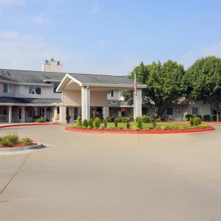 A two-story building with a circular driveway surrounded by neatly trimmed bushes and trees.