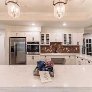 A modern kitchen with white cabinets, an island, and stainless steel appliances, highlighted by elegant pendant lights and a decorative backsplash.