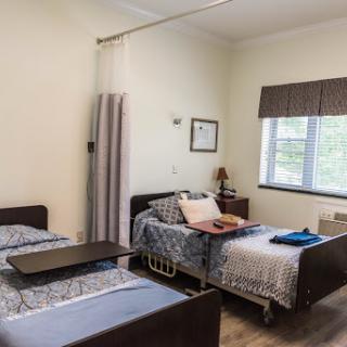 A cozy hospital room featuring two beds, a window with curtains, and essential furnishings for patient comfort.