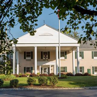 A colonial-style building with large columns and a well-maintained lawn surrounded by trees.