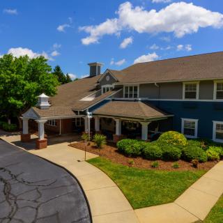 A charming two-story house surrounded by lush greenery under a partly cloudy sky.