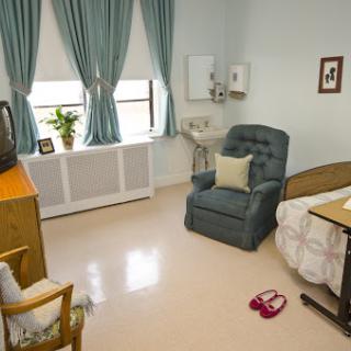 A cozy hospital room featuring a bed, comfortable chair, and a small TV.