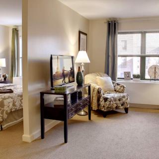 A cozy interior featuring a living area with a TV, comfortable chair, and lamp, adjacent to a bedroom.