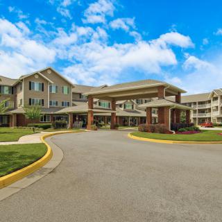 A view of a large residential building with a circular driveway and neatly maintained landscaping under a partially cloudy sky.