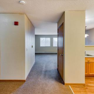 A spacious hallway with carpet flooring leading to a brightly lit room with wood accents.