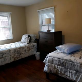 A cozy bedroom with twin beds, a dresser, and natural light from two windows.