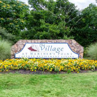 Entrance sign for the Village at Harbor Pointe, surrounded by flowers and greenery.