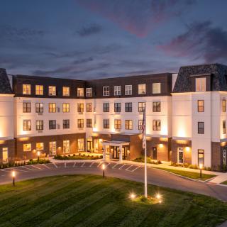 A well-lit hotel building at night with manicured lawns and a circular driveway.