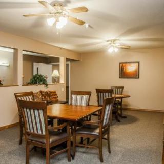 A cozy dining room with wooden tables and chairs, warm lighting, and ceiling fans.