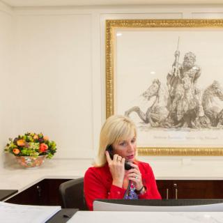 A woman in a red jacket talks on the phone at an office reception desk.