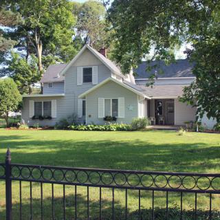 A charming house with a lush green garden and tall trees, surrounded by a decorative fence.