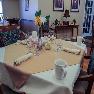 A neatly set dining table with a flower centerpiece, glasses, cups, and napkins in a cozy room.