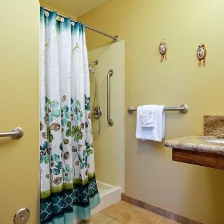 An accessible bathroom with a floral shower curtain, handrails, and yellow walls.